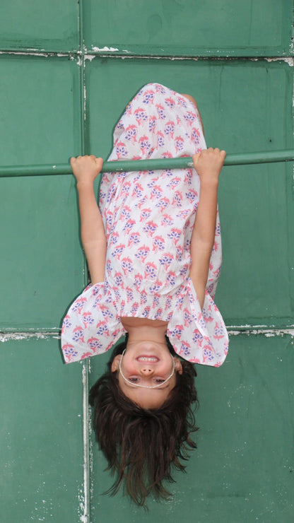 Child in a floral dress hanging upside down against a green wall
